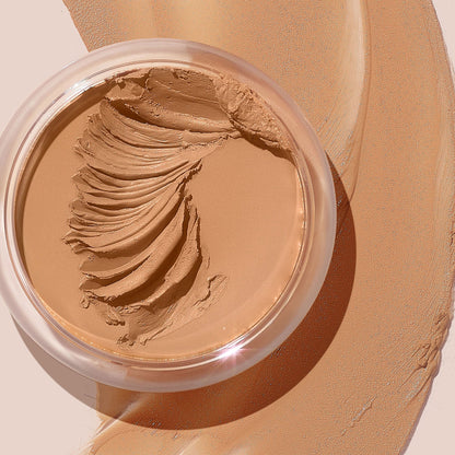 ColourPop SOL Face & Body Bronzing Balm in shade Light sits in a clear round jar with creamy swirls, with warm golden-tan balm swatched around it on a beige surface, showcasing a smooth, blendable texture and natural dewy finish.