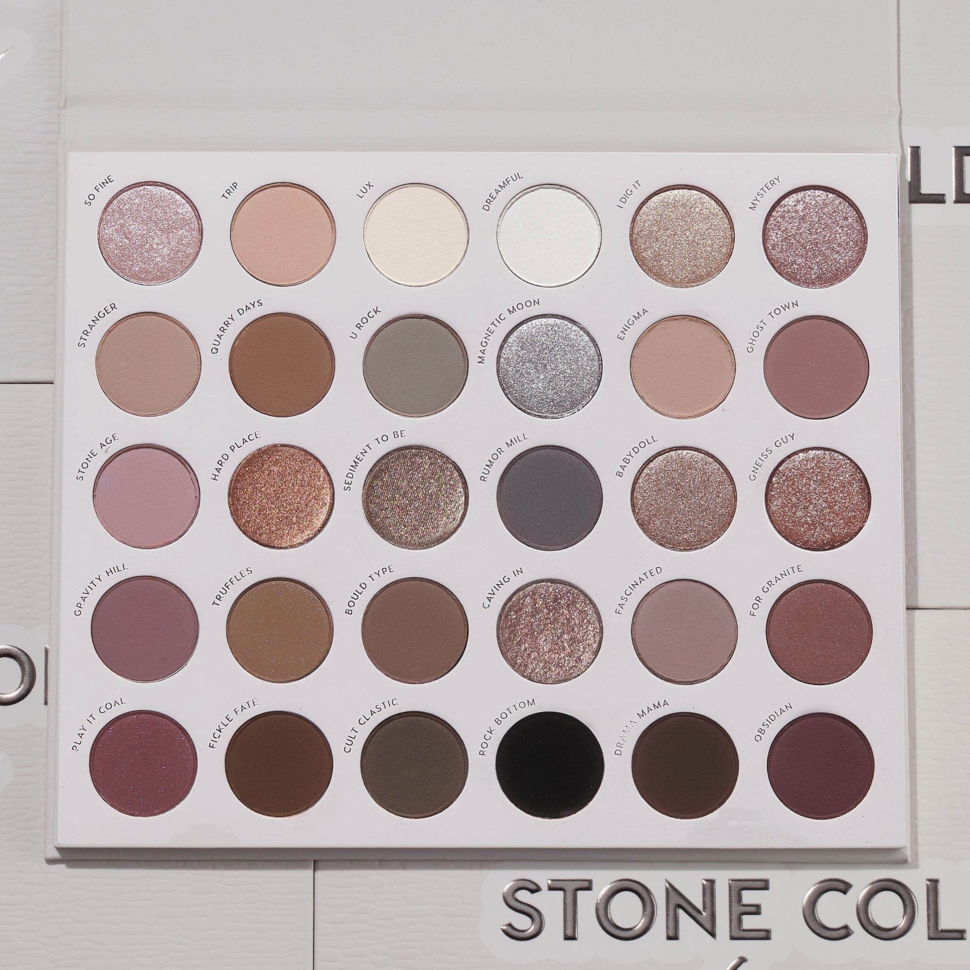 Stone Cold Fox ColourPop Shadow Palette lies open, displaying 30 cool-toned neutrals - taupes, mauves, grays, and browns - in matte, shimmer, and metallic finishes inside a white case on a light textured surface with the logo partly visible.