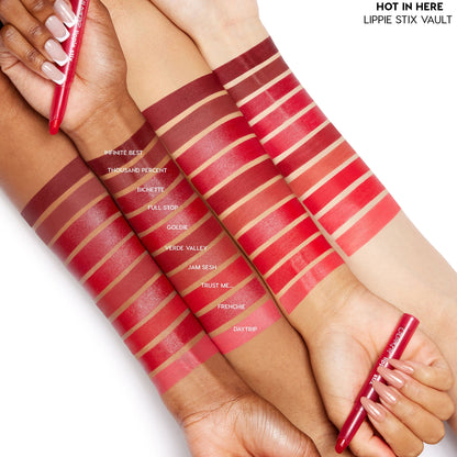 ColourPop Lippie Stix Hot in Here Vault swatches sweep across three skin tones, showing 10 reds from deep burgundy to bright coral (Infinite Best to Daytrip), as hands hold red Lippie Stix pens on a white studio background.