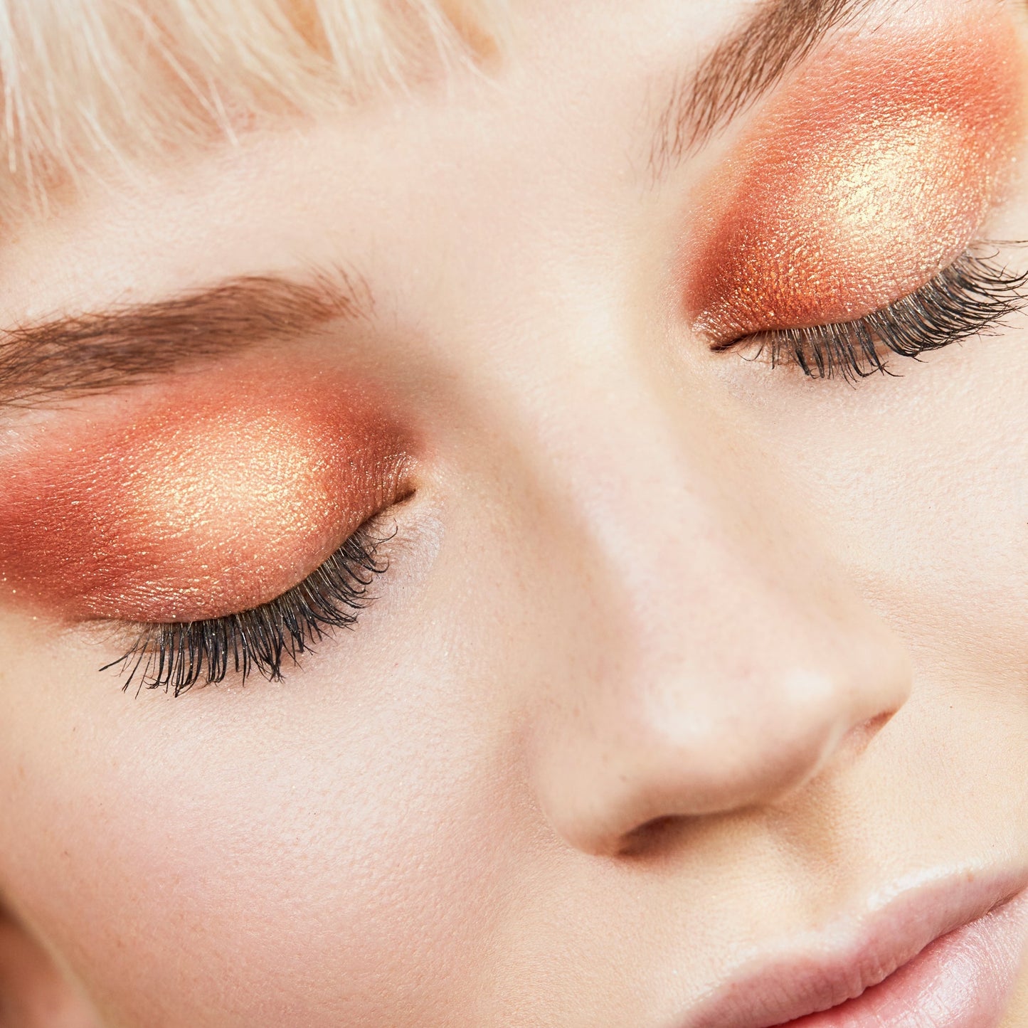 ColourPop Super Shock Shadow in Pledge Class shimmering across closed eyelids, showing a warm copper-to-peach gradient with golden metallic sparkle and soft lashes in a close-up beauty shot.
